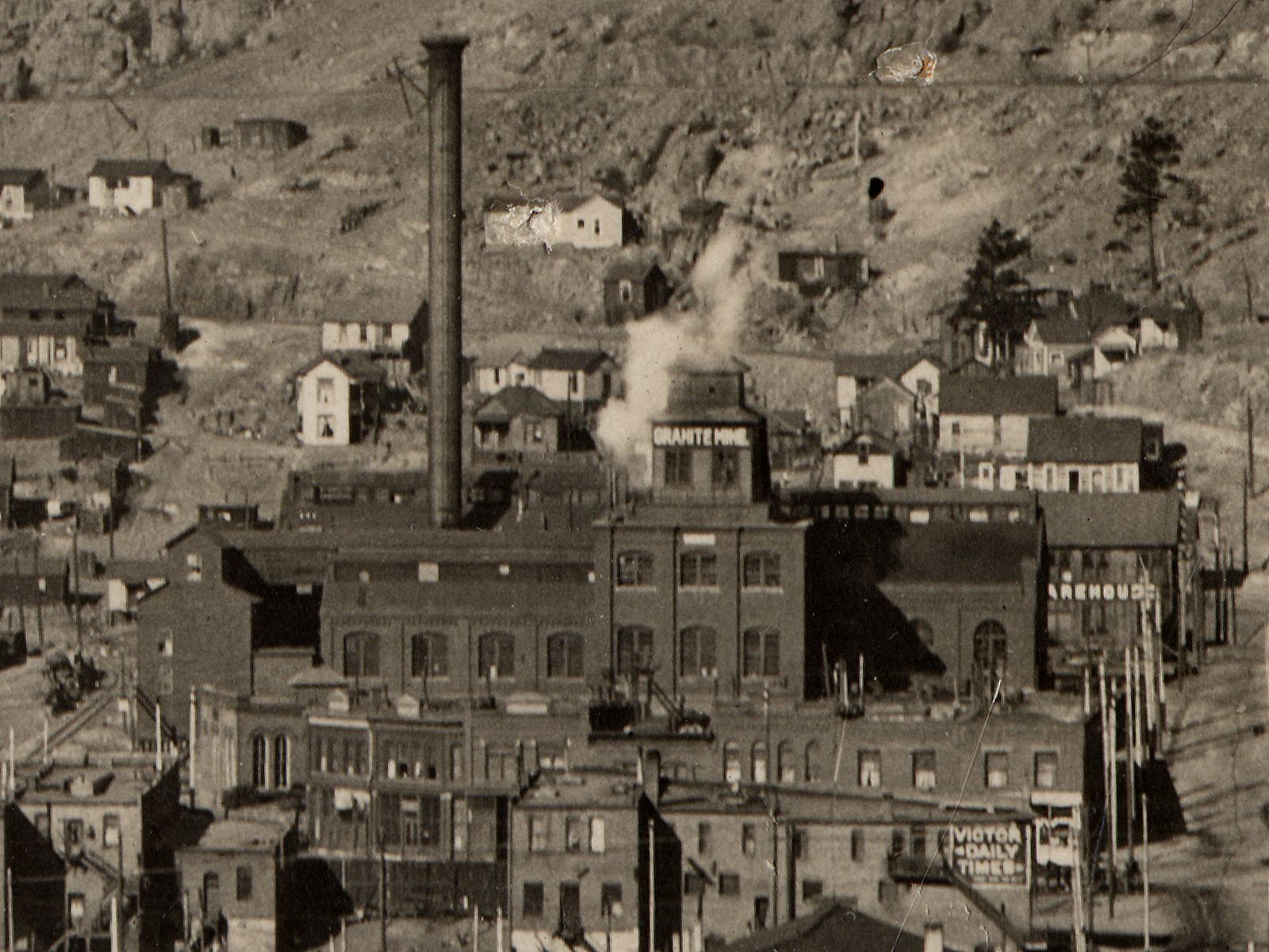 This view, cropped from a long-distance view, shows the eastern face of the Gold Coin Mine in Victor in all its glory, after it sold to the Granite Gold Mining Company, as it is now marked as being the Granite Mine. In early December of 1905 it was in mining journals published news that the Gold Coin had been sold, as part of a 13 acres' land deal, to the Granite company, who seems to have leased the property at least half a year before that time.
When looking at this image it is no wonder Victor was named City of Mines, as this is smack into the town, and no wonder they needed the Columbine-Victor tunnel to get rid of waste rock as there is no room left here for any dumps. In the background is two levels of Midland Terminal grade seen, the lower one is the spur down to its Victor station, and the upper one is the mainline, seen just behind the top of the chimney.