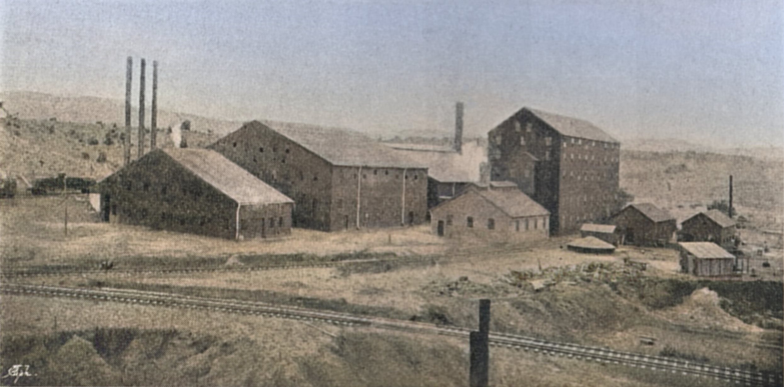 This sadly bad view of the El Paso Mill in Florence is one of very few known views of this mill that was located southeast of the town of Florence, and which was to treat gold ore from the Cripple Creek Mining District using the Chlorination Process.
   While this view appears in an August 1898 publication, I can use the only Sanborn Map that shows this mill, the January 1900 Sanborn Fire Insurance Map, to see that the direction of the view is looking southwest. The railroad line in foreground is dual gauge and is the main track for the branch line that served this and a second chlorination mill, in addition to a smelter. I think the outbound track is the spur that goes back to the high narrow structure that Sanborn call the Chlorination Building. The Inbound track is partly seen at left edge about middle top/down, where an oil tank car is seen. On the hill behind that car, outside the view at left, there was an oil-tank according to the Sanborn map, and text in the article where this image appeared.
   Building where the 3-smokestacks appears at left are the Power Plant House for most part, and then the large high one is the Crusher and Dryer structure, followed by a structure holding Bedding Floors, Roasters and Cooling area. The even higher, narrower structure more to the right is, as said, marked as being the Chlorination Building with a Belt House and Refinery more towards the photographer. Further right there is a Carpenter and Blacksmith shown as smaller structures, with a more shed like structure closer to the photographer. There is no trace of the Concentrator Building seen on the Sanborn which should been visible at the right-hand side, indicating it was a later construction then this 1898 source had.
   I did procure the colored version of this image. Source was gray-toned, or in common speech black & white. Used an online service and tweaked and worked with image to get what looks best to my eyes for the moment.