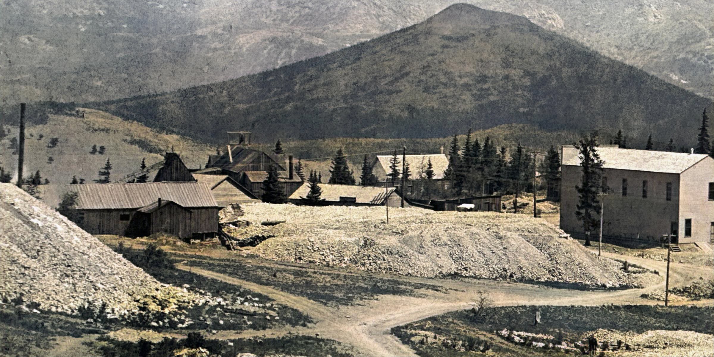    * Old Pharmacist Mine is seen at far left with a triangular peaked Cupola and a longish narrow structure as a Shaft House, said to be an Incline type of shaft. Quite an extensive dump spread out east of the structure. The Shed poking out towards the photographer is per Sanborn Fire Insurance map of 1900 (Sheet 14, Victor set) for the Blacksmith. The dump in foreground obscuring the west end of the shaft house is part of the Zenobia dump.
   * Beyond the Pharmacist, into the image just at right, is the Burns Mine with part of a head frame poking up from the roof. What is in the image is not fully fitting the 1900 Sanborn map, but that mine was not included in the 1896 maps and the 1908 edition shows a different look altogether.
   * A rectangular shaped structure and marked with a cross is seen further right, a church in Altman, also seen on the 1908 Sanborn map, marked as R.C. Church, not used by then.
   * The structure that was later to hold the Geo. McMillan Grocery Shop marked out in other photo's with an extension not seen in this photo is located at southwest end of the main-street of Altman, or far-right in this cropped view.
   I did procure the colored version of this image. Source was grey-toned, or in common speech black & white. Used an online service and tweaked and worked with image to get what looks best to my eyes for the moment.