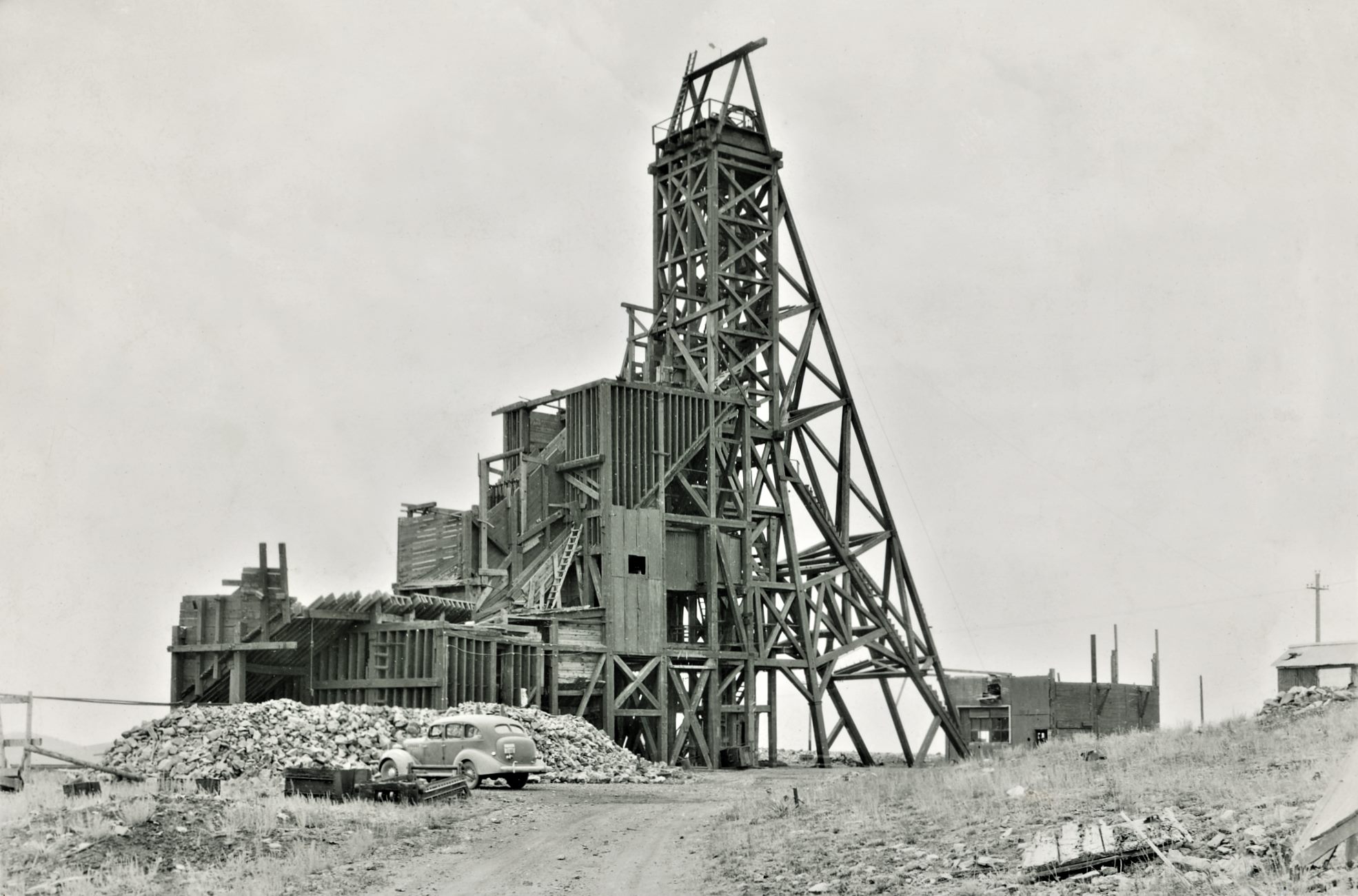 This somewhat enhanced view at the exposed Huge Head-Frame/Gallows-Frame of the old Stratton Independence Mine on Battle Mountain, outskirts of Victor, Colorado, show quite well how Huge the whole structure was! Dating this view is hard, I think it is from around 1940, but I do not know. There is a car parked below this mine structure, and that seems to have a License-plate of 43-660 but I can't tell what else it might have written above the numbers, so I can't date the image from that either…
   The whole structure is quite massive, and all in wood it appears! Hard to imagine all this at one time enclosed in a massive Shaft-house type of structure, as I assume this is as it was built inside the structure back in the days. The left most parts, with the various bins I do think is more recent then the headframe itself, but I dare not say anything as this is beyond my knowledge.