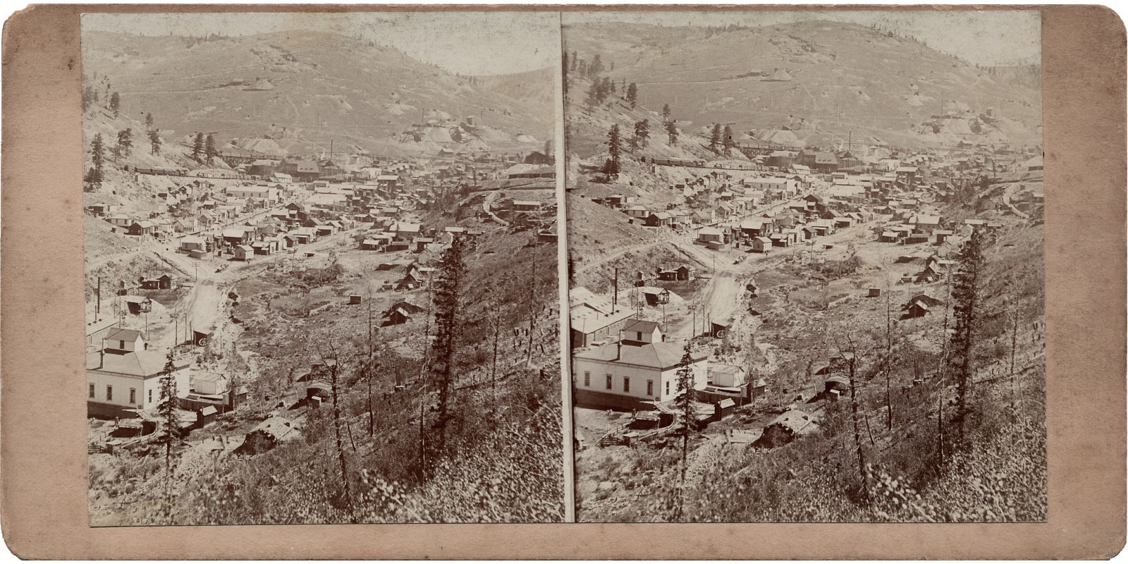 This view from an unmarked Stereoview is showing the town of Anaconda with the School House and part of the Hartzell Mill in the foreground left. In the background is Gold hill and some of its mines, while the town itself is located near the Anaconda mine. Anaconda mine is about 1/3 down from the top and about middle-of-view in the left/right direction. About halfway up on the left side is the Ore-house of the Blue Bell mine just above the school house cupola.