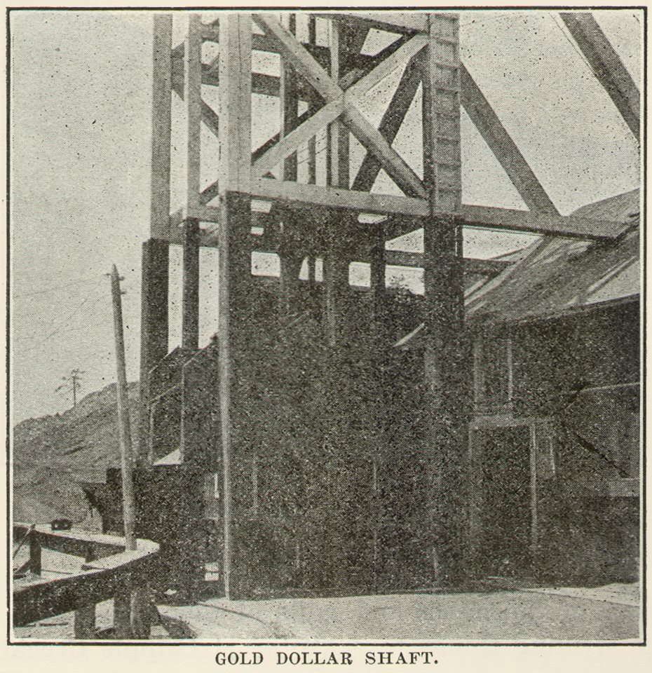 This view of the Gold Dollar shaft show how surface tramming is done by electric cars using 3-phase, 550-volt motors. The three trolley wires are mounted in a channel built of boards which can be seen about two feet above the ground at the left of the track in the view. There is not much likelihood of anyone coming in contact with these wires accidentally, protected as they are in the deep channel by the overhanging boards.
   Sadly, the image quality is not good, so it is not easy see details, but there is standing one of those cars at the chute where the underground materials are dumped from the shaft.